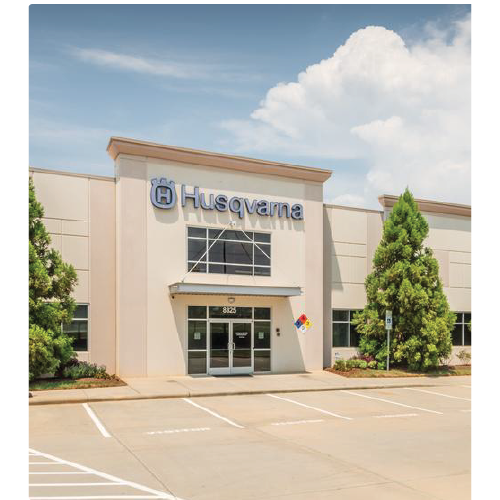 Exterior of a Husqvarna building with the company logo above the entrance and neatly trimmed trees on each side.
