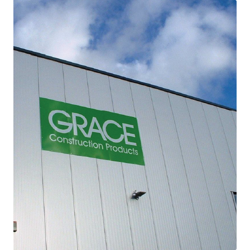 Green sign on white exterior wall reading 'GRACE Construction Products' under a partly cloudy sky.